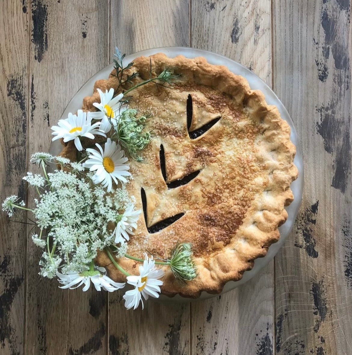 Homemade pie topped with daisies on a rustic wooden table